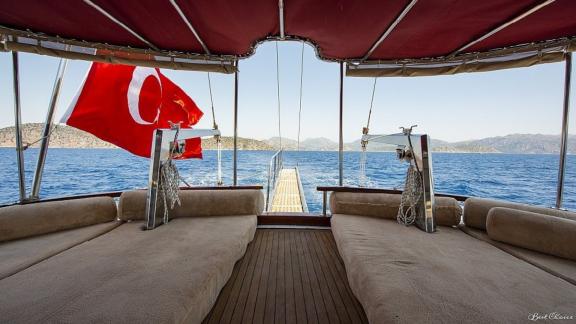 Rear deck of the gulet Vesta 1 Sevil with comfortable seating and a view of the Turkish flag and the sea.